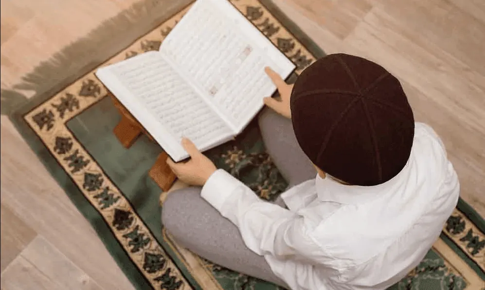 Boy memorizing the Quran on a prayer mat