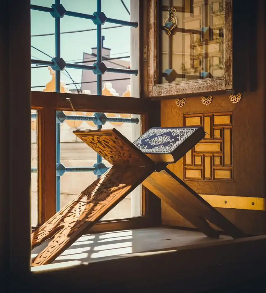 Quran on a carved wooden rehal by a sunlit window