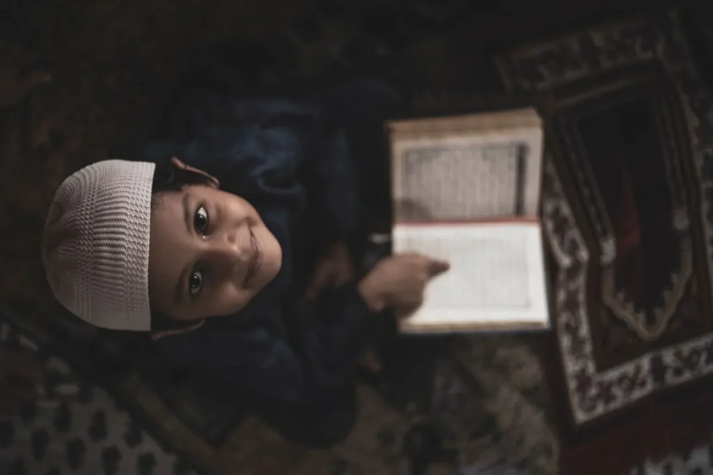 Smiling young boy reading the Quran on a prayer mat